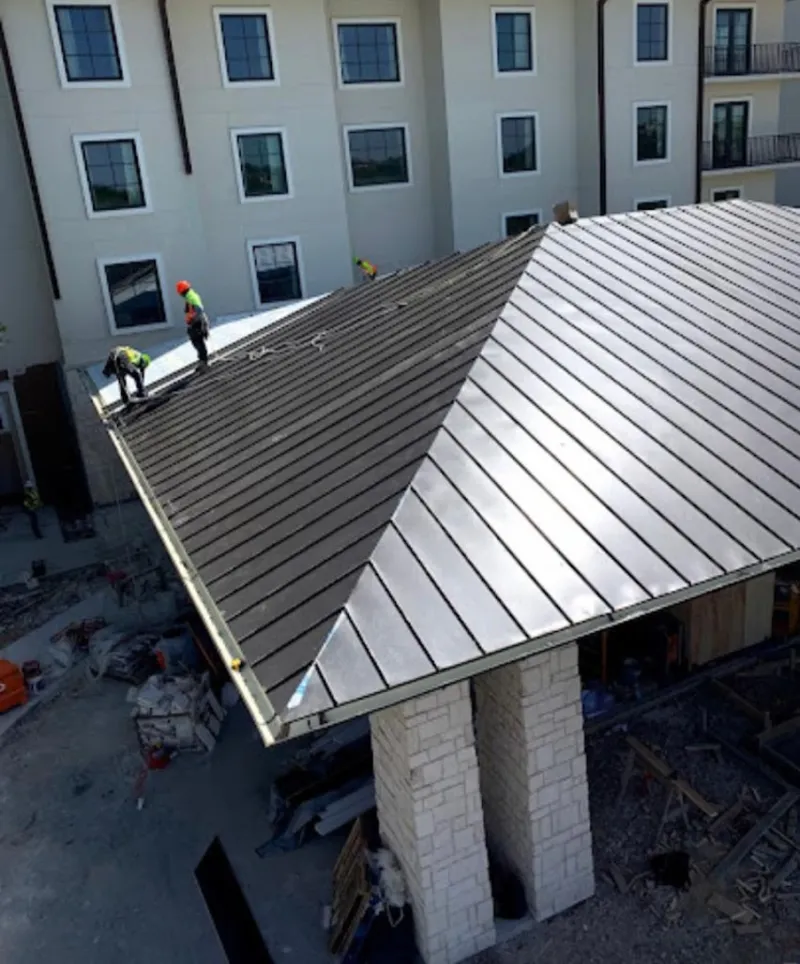 Crew installing standing seam metal roof panels on a commercial project in Gilberts